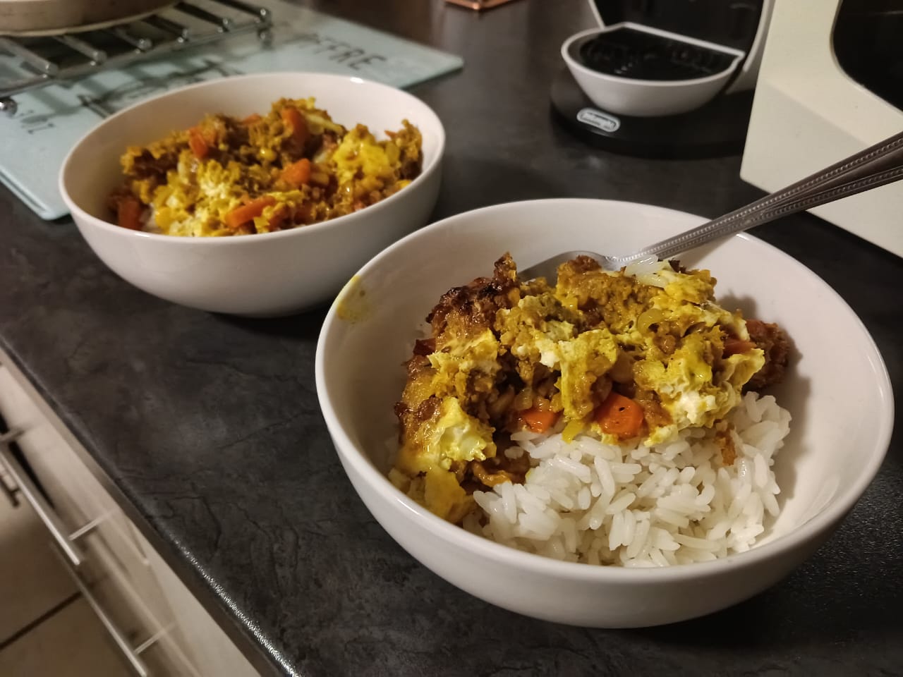 Two white bowls with rice and portions of bobotie inside